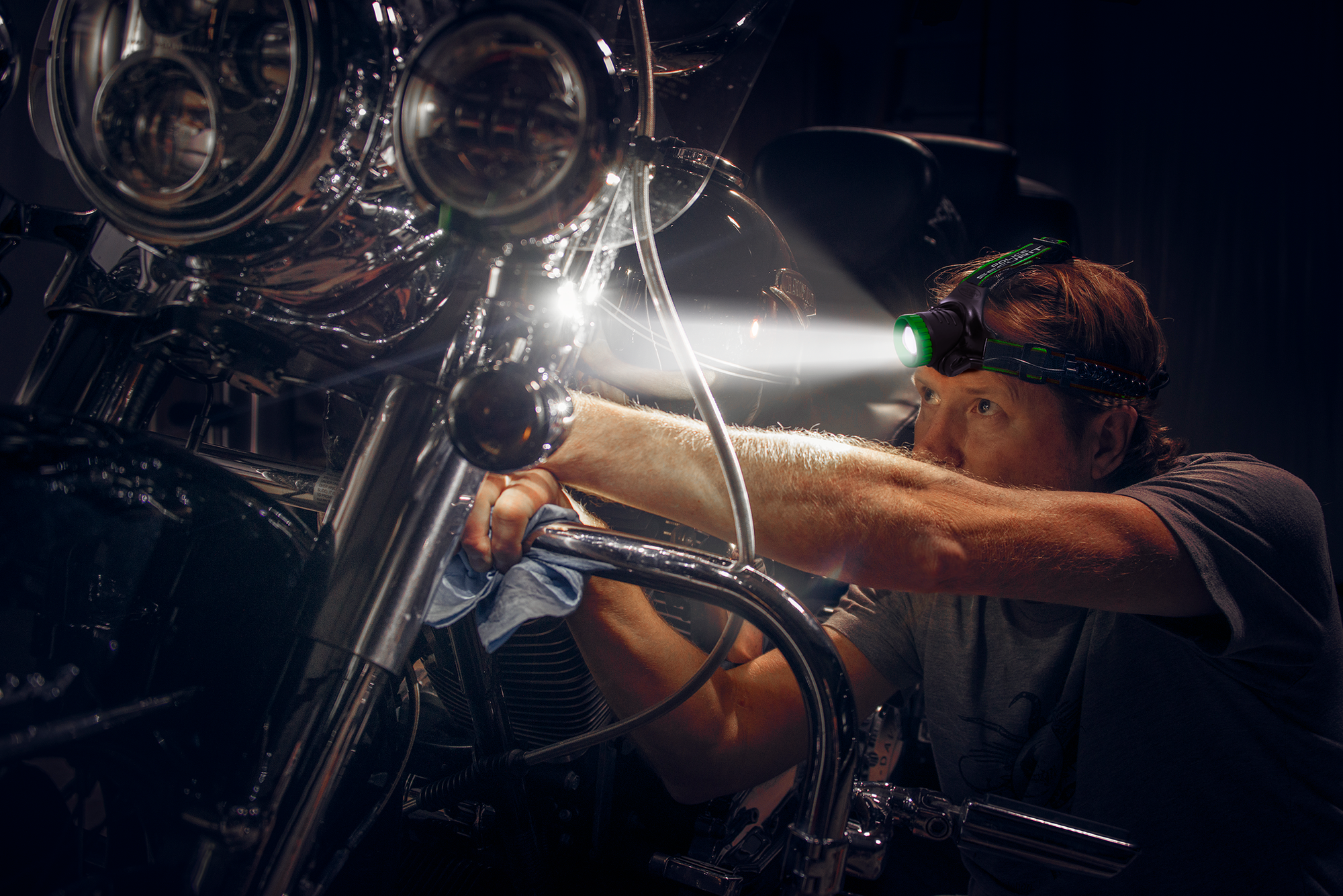 man wearing bright headlamp working on motorcycle