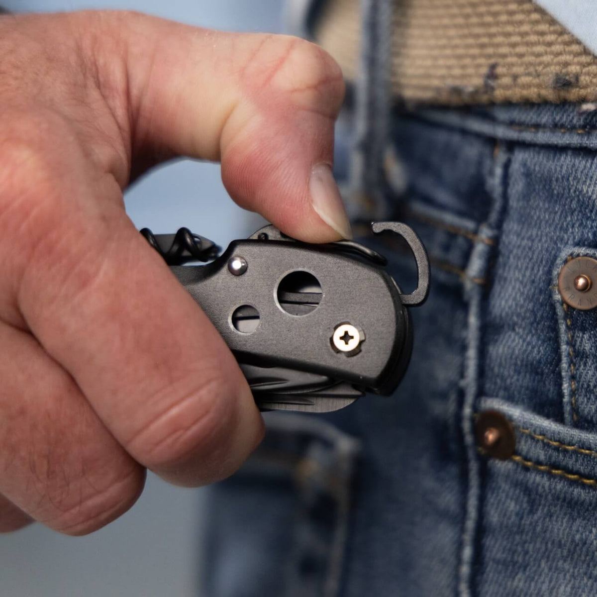 A person's hand holds the Scout multi-tool pocket knife and shows the carabiner clip being opened