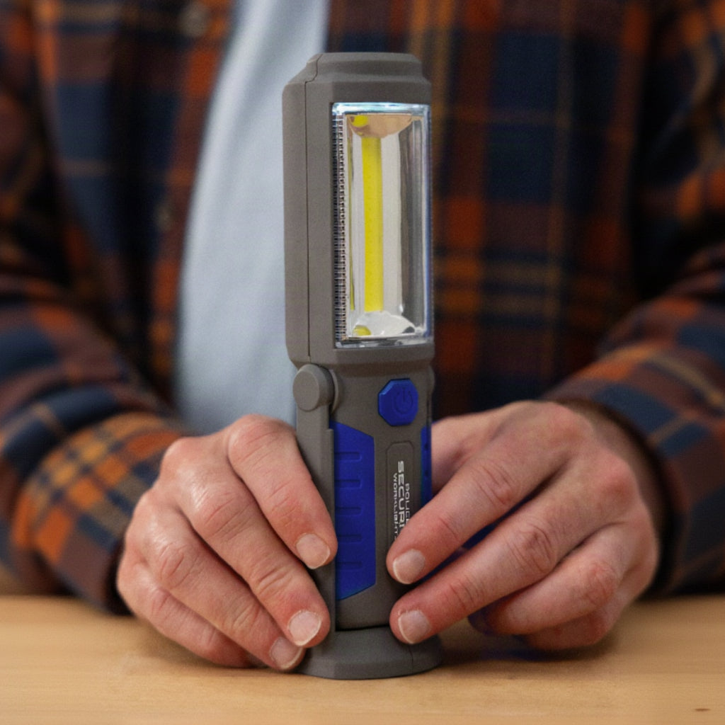 A man in a plaid shirt holding the Proflex Deluxe work light on a wooden workbench