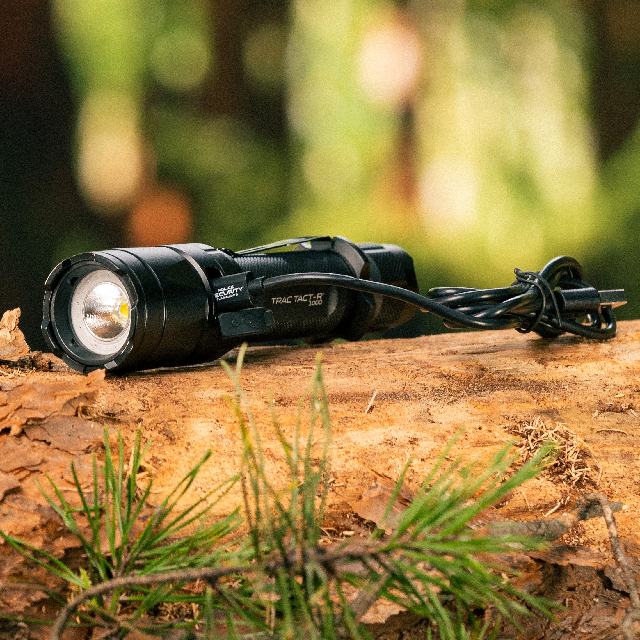 The Police Security Trac Tact RX lying on a log with the charging cable plugged in