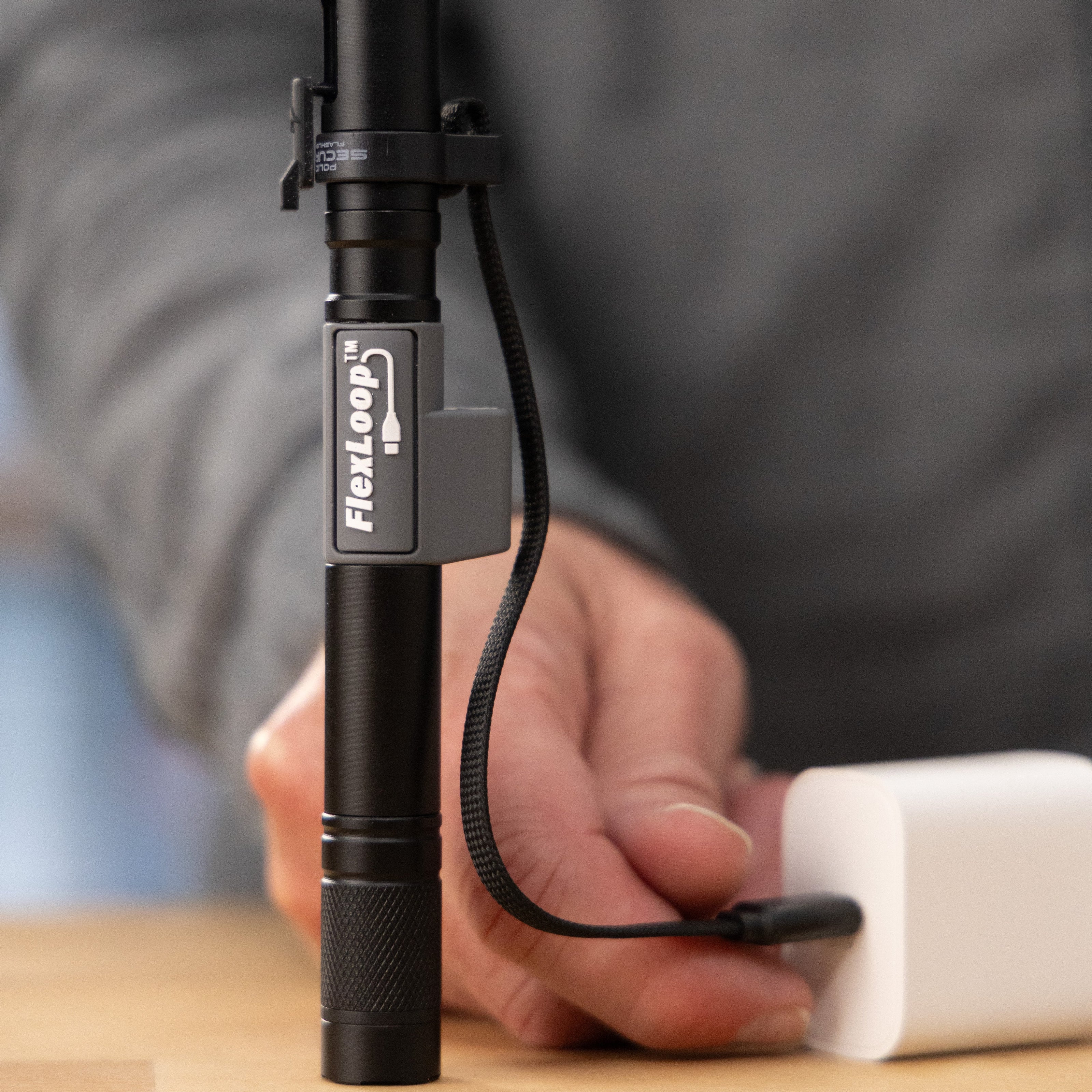Black Flexloop Aura R flashlight held by a person being plugged in to an AC adapter with a blurred background