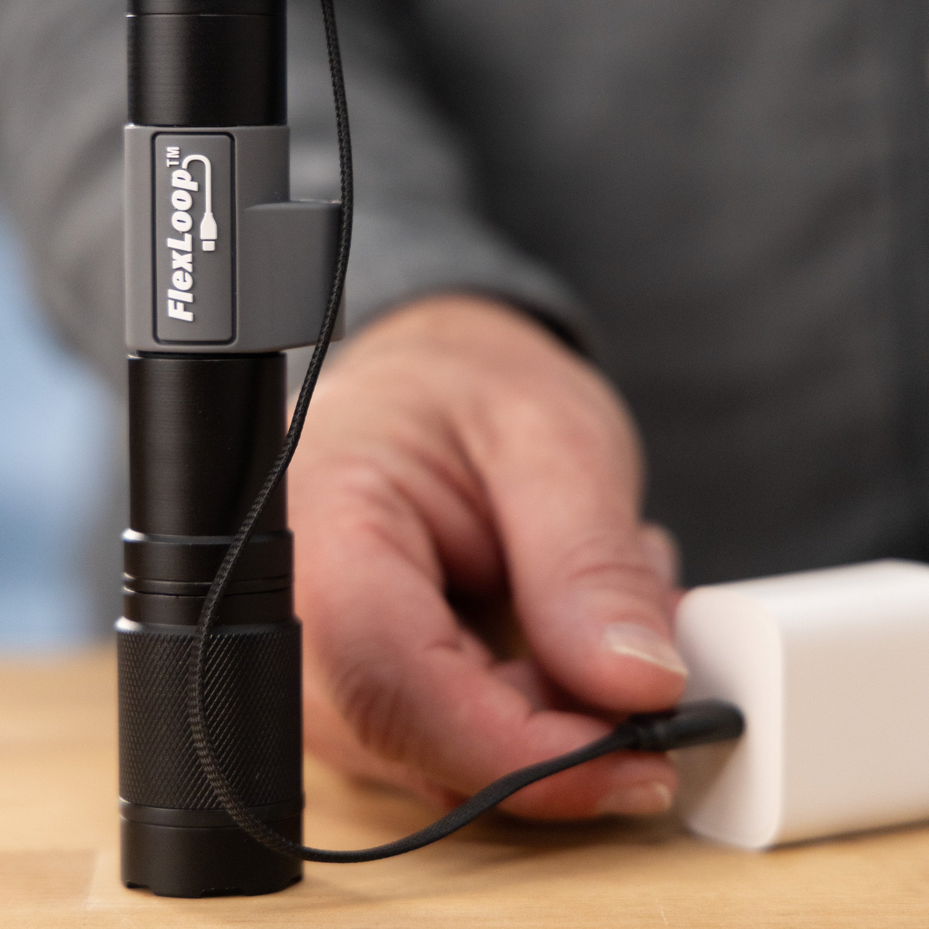 Black Aura RX flashlight with FlexLoop branding on a wooden surface, held by a hand.