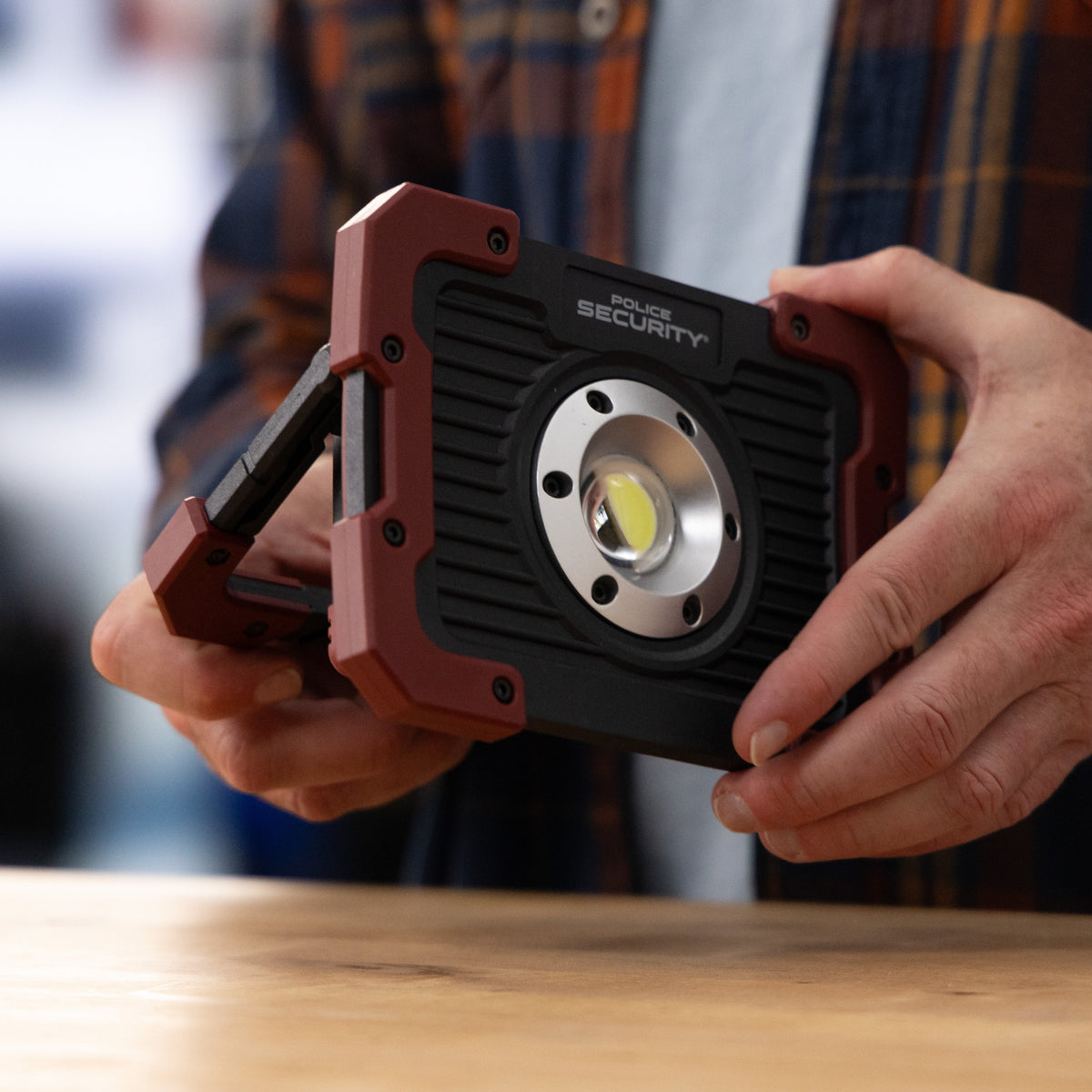 A person holding a rugged black and red Kickstand-R LED work light with the set against a blurred background.