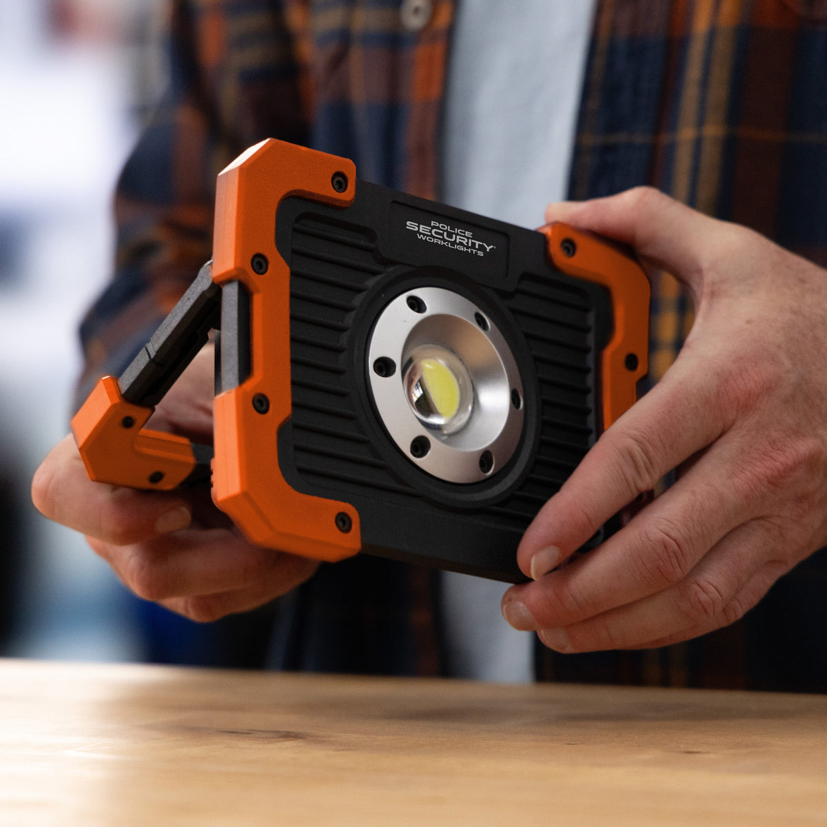 A person holding a rugged black and orange Kickstand-R LED work light with the set against a blurred background.