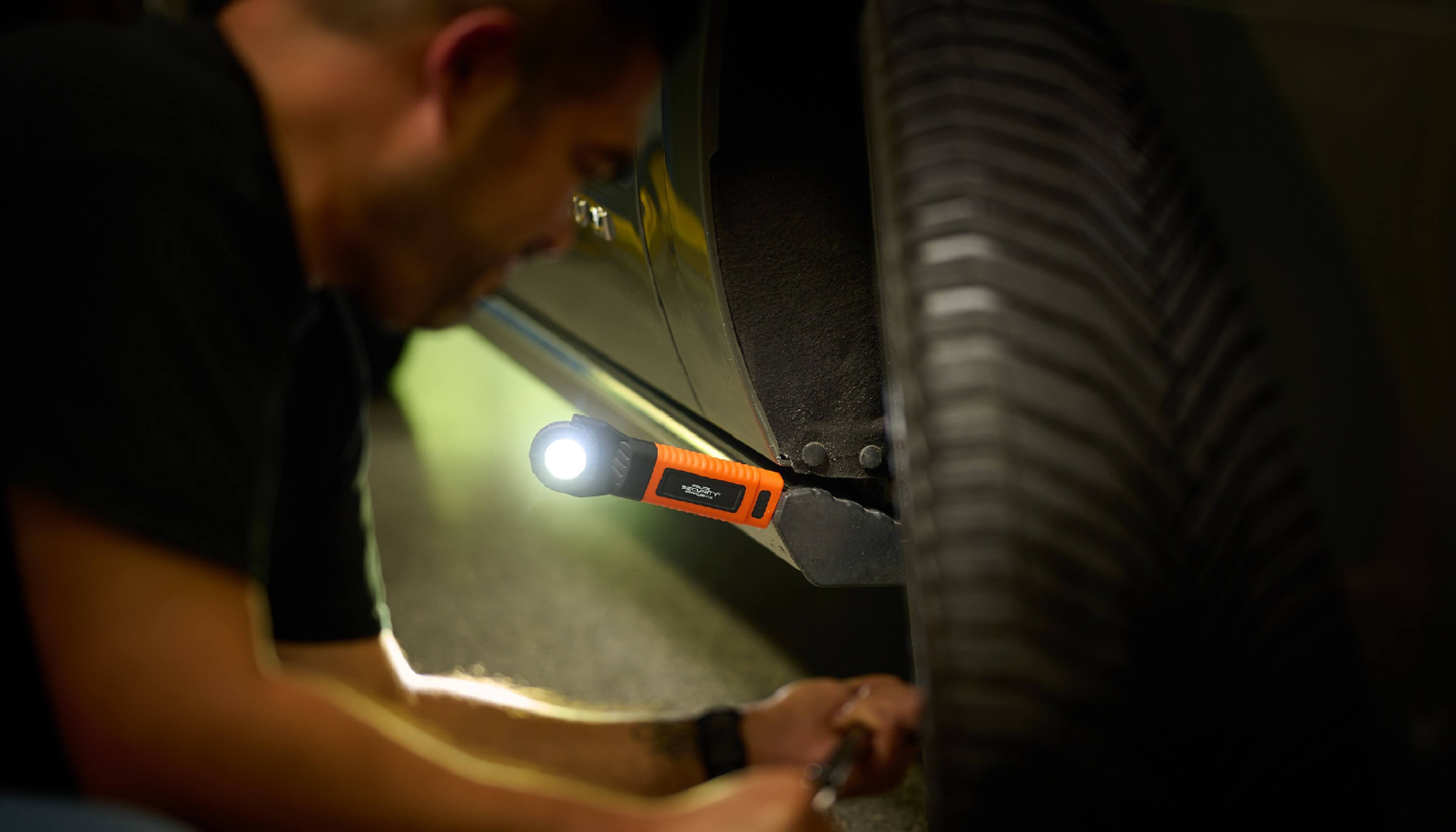 A man uses a magnetic work light to illuminate his car wheel while he does automotive work