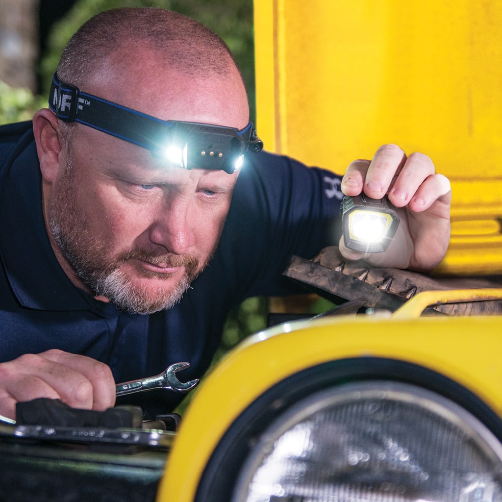 A man fixing his jeep hands free due to the headlamp he's wearing and the removable light