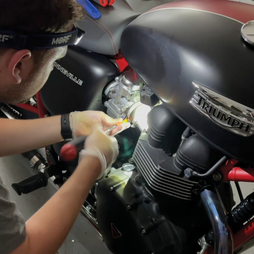 an image of a man fixing a motorcycle with both hands and lighting it with a headlamp