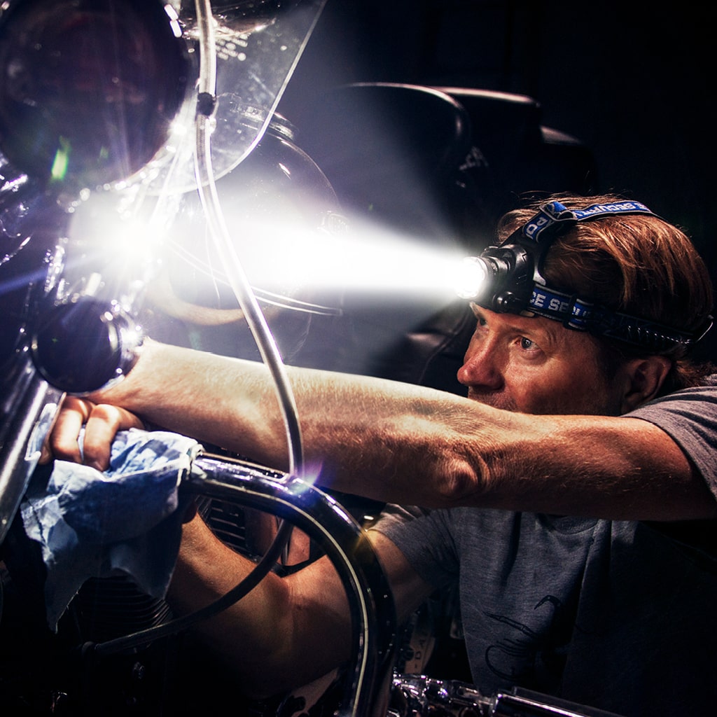 A man trying to fix his motorcycle with a headlamp that's blasting a bright light