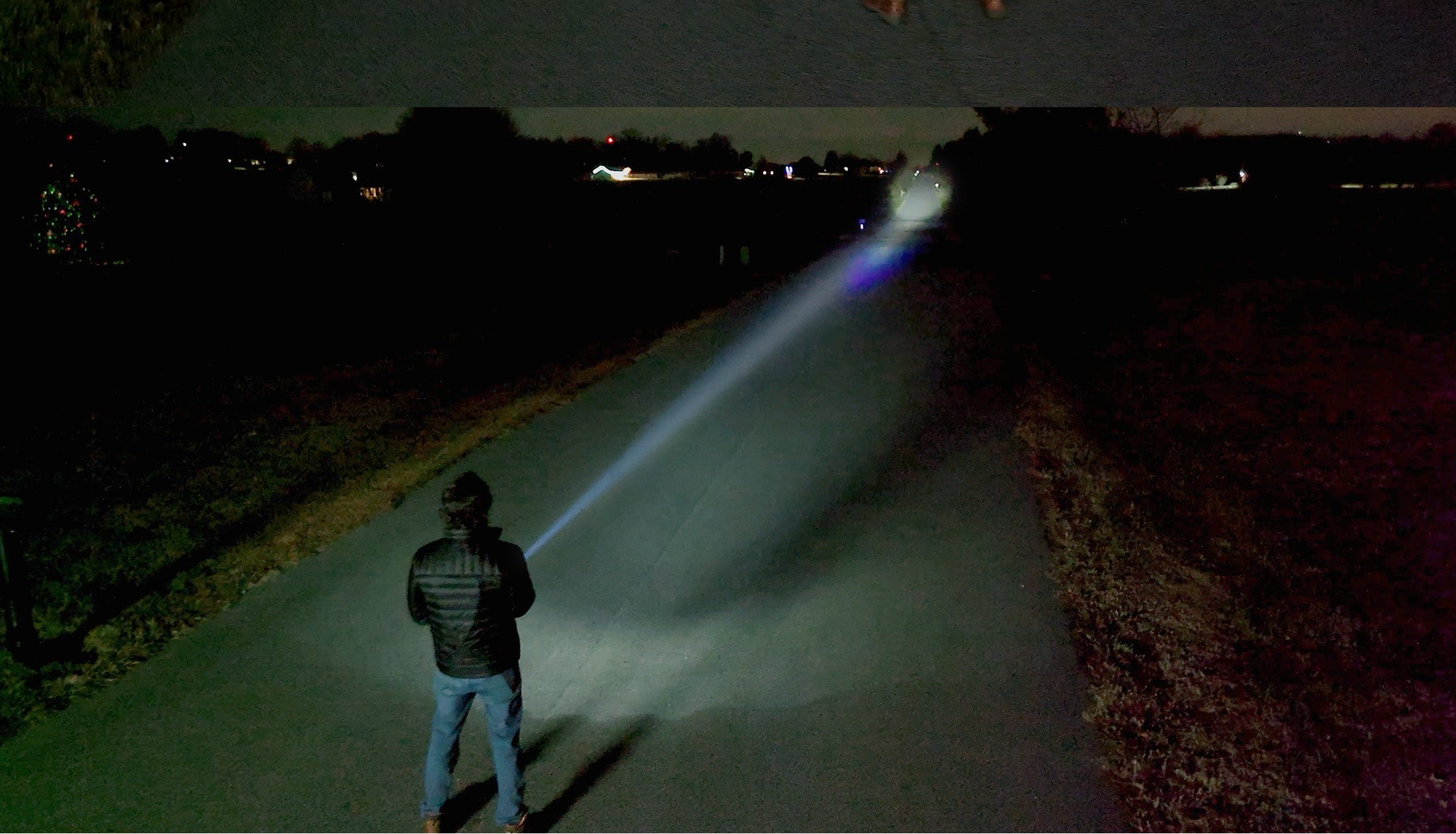 A man using a flashlight to shine a tight spotlight beam down a road for a great distance