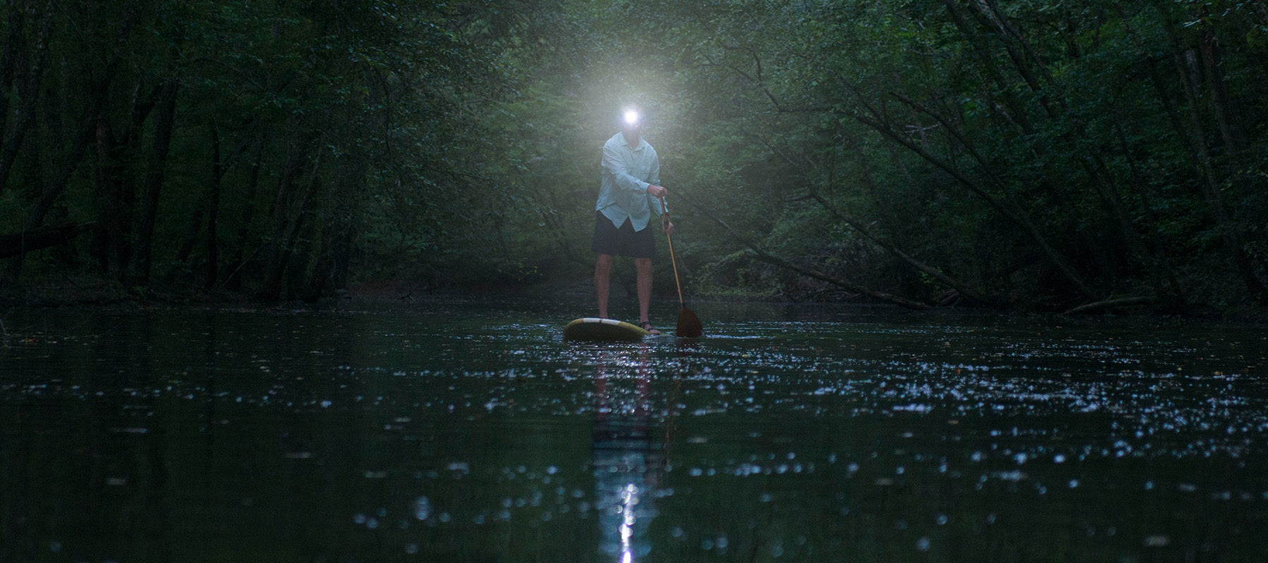 an image of a man paddleboarding on the river while wearing a headlamp