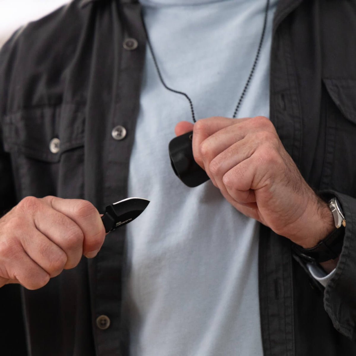 A man pulling a small knife out of the sheath worn around his neck
