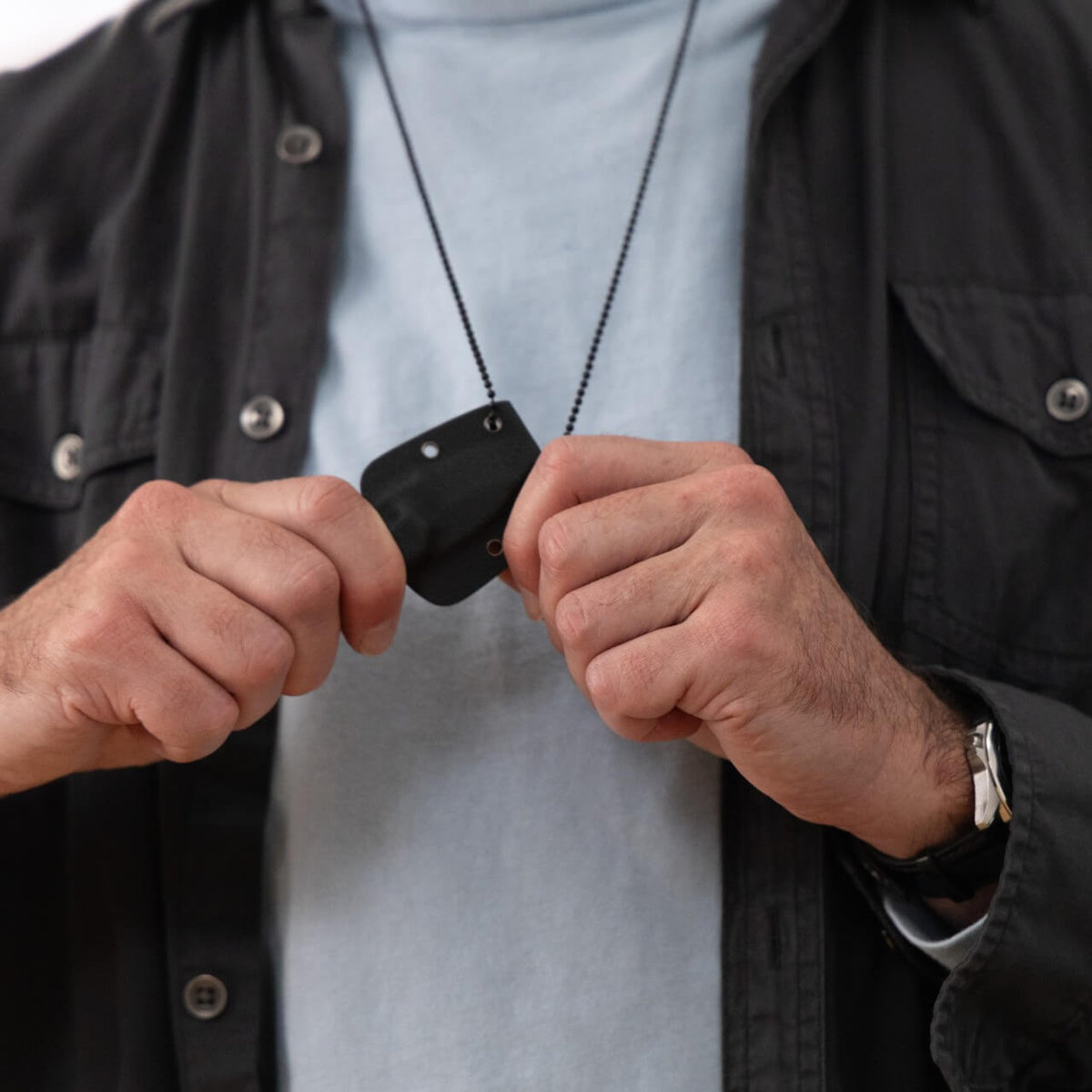 A man holding on to a small knife in a sheath hanging from a chain around his neck
