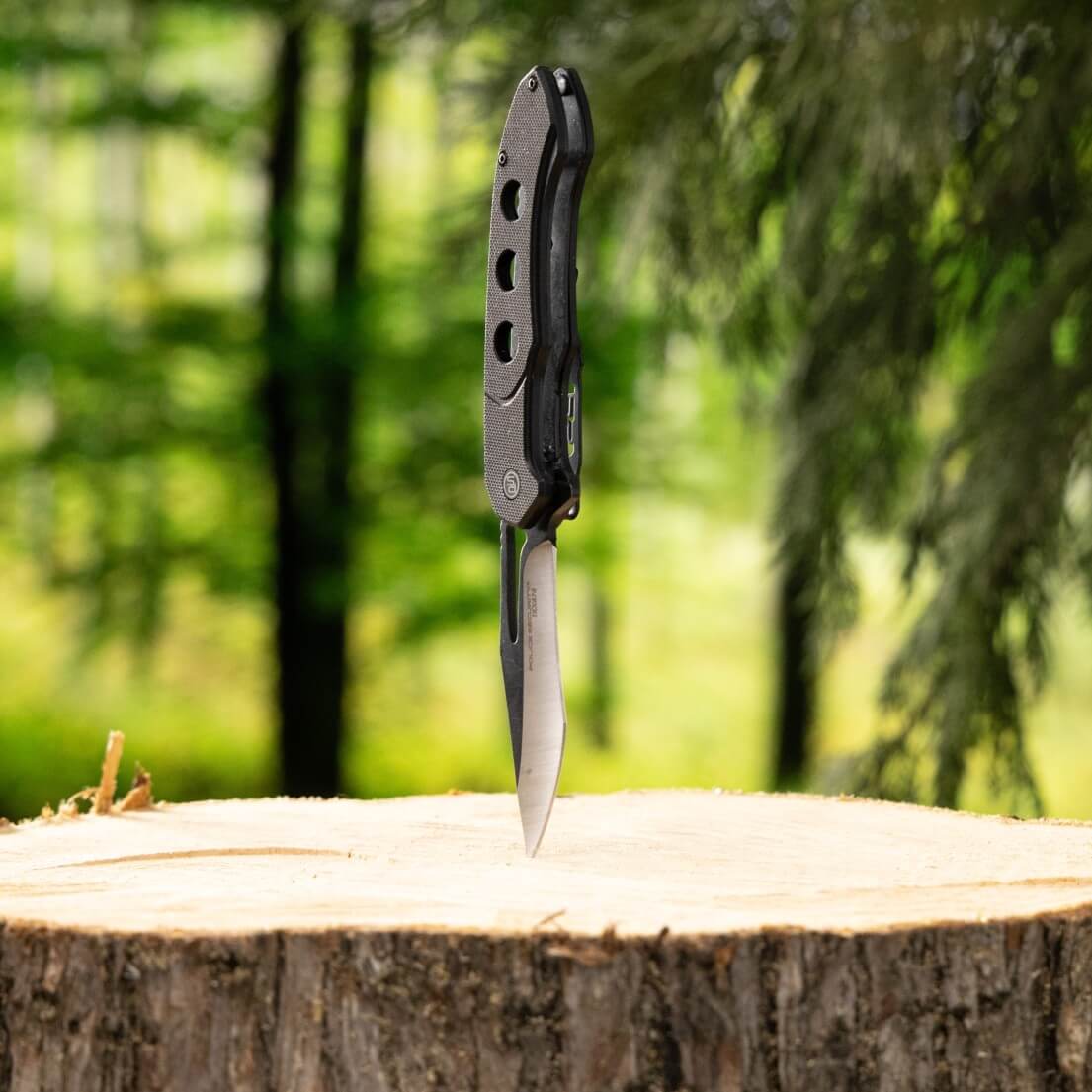 The TKX Pro pocket knife stabbed into a stump, showing the bottom angle of the knife 