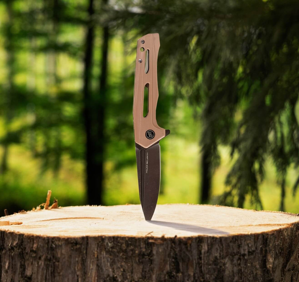 The TKX Elite folding knife with brown handle and black metal blade stabbed into a stump with trees in the background