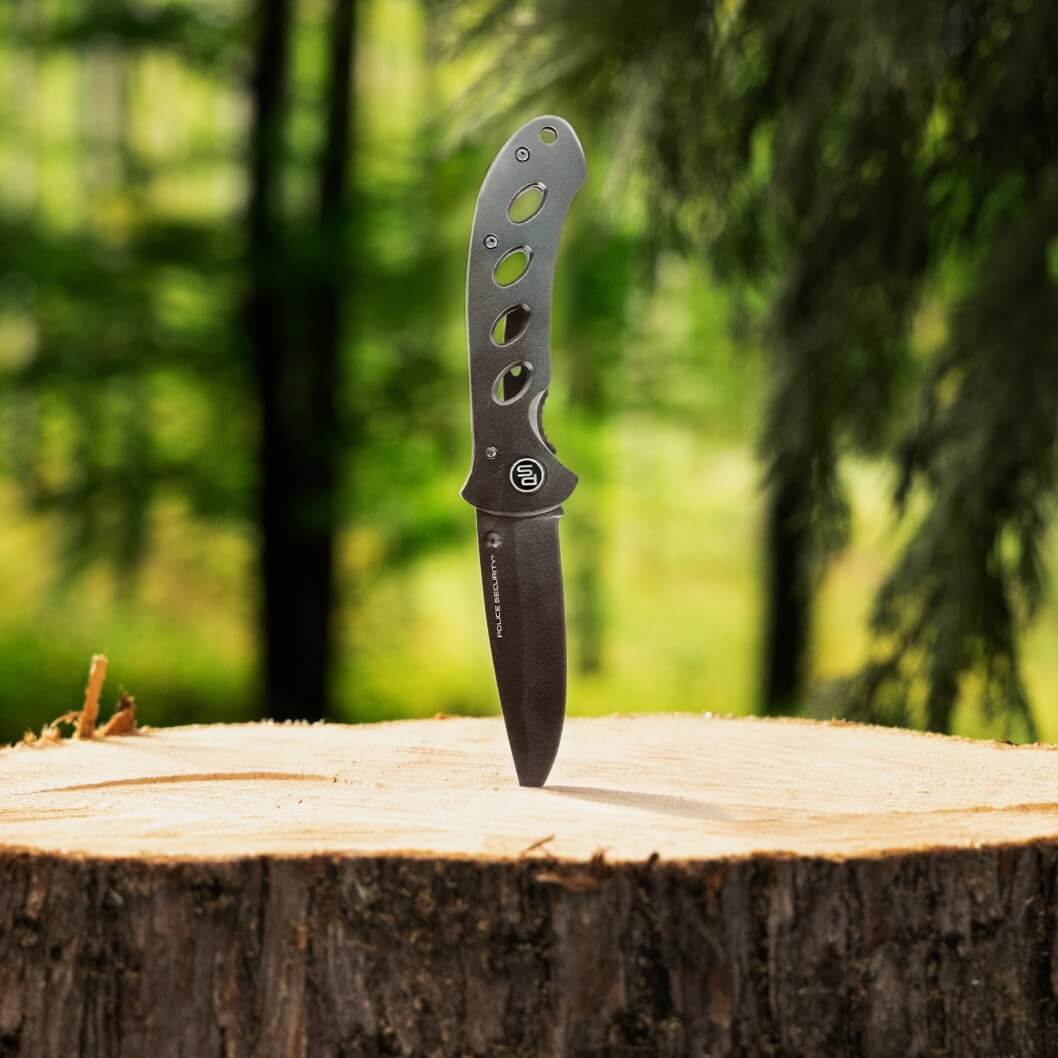The TKX Edge pocket knife from Police Security stabbed into a stump with woods in the background