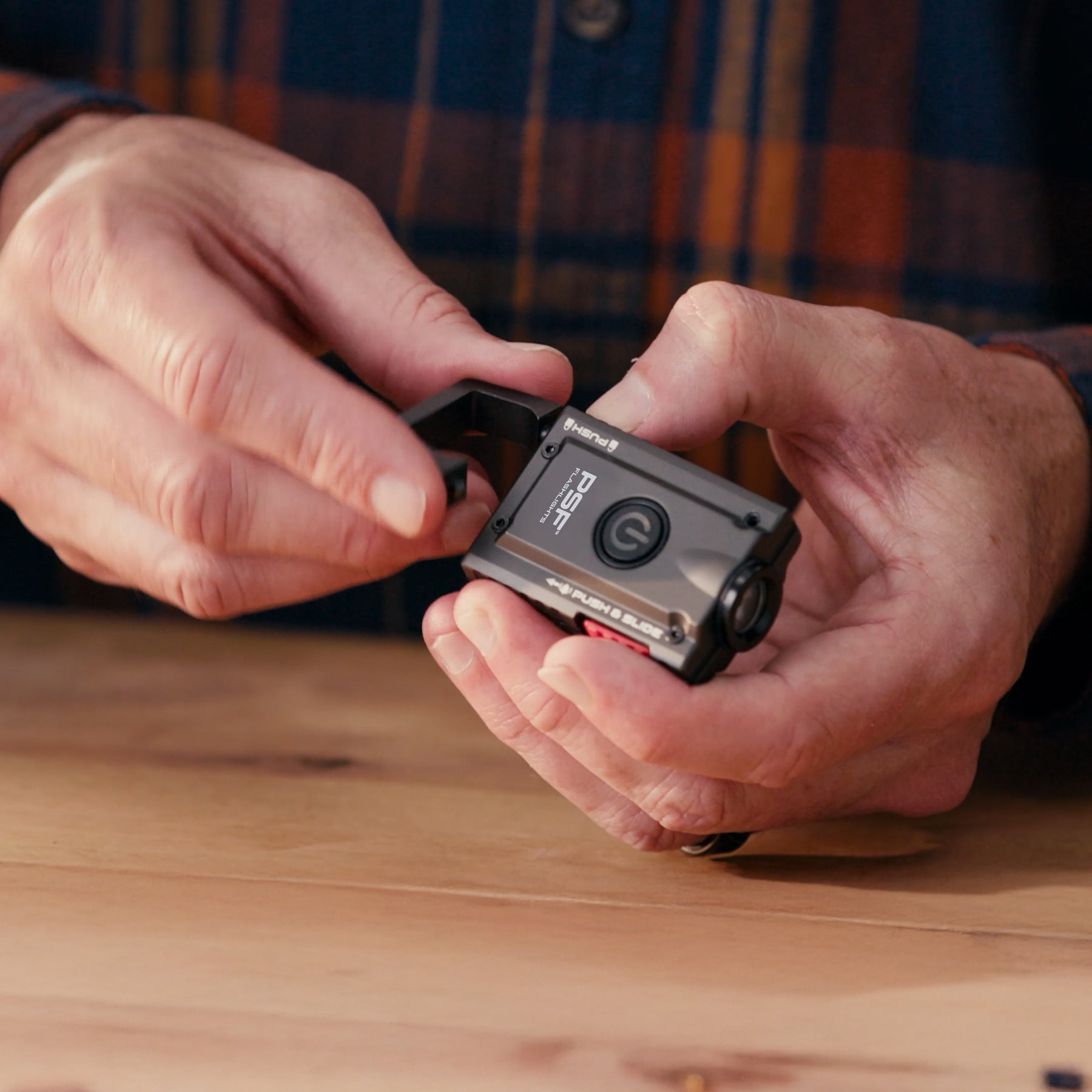 Person holding a small Alert120 keychain flashlight on a wooden surface