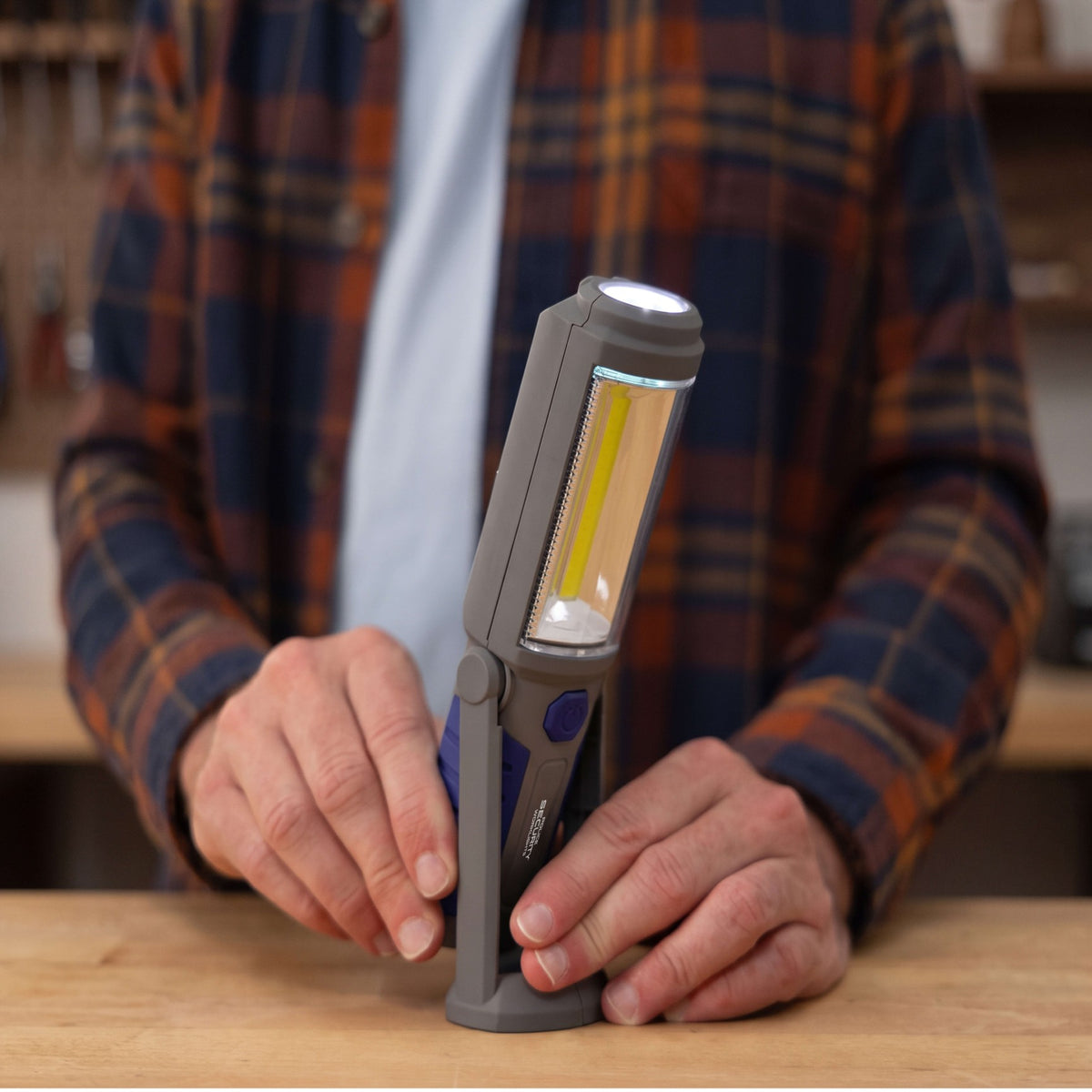 A man in a plaid shirt tilting the Proflex Deluxe flashlight on a wooden work bench