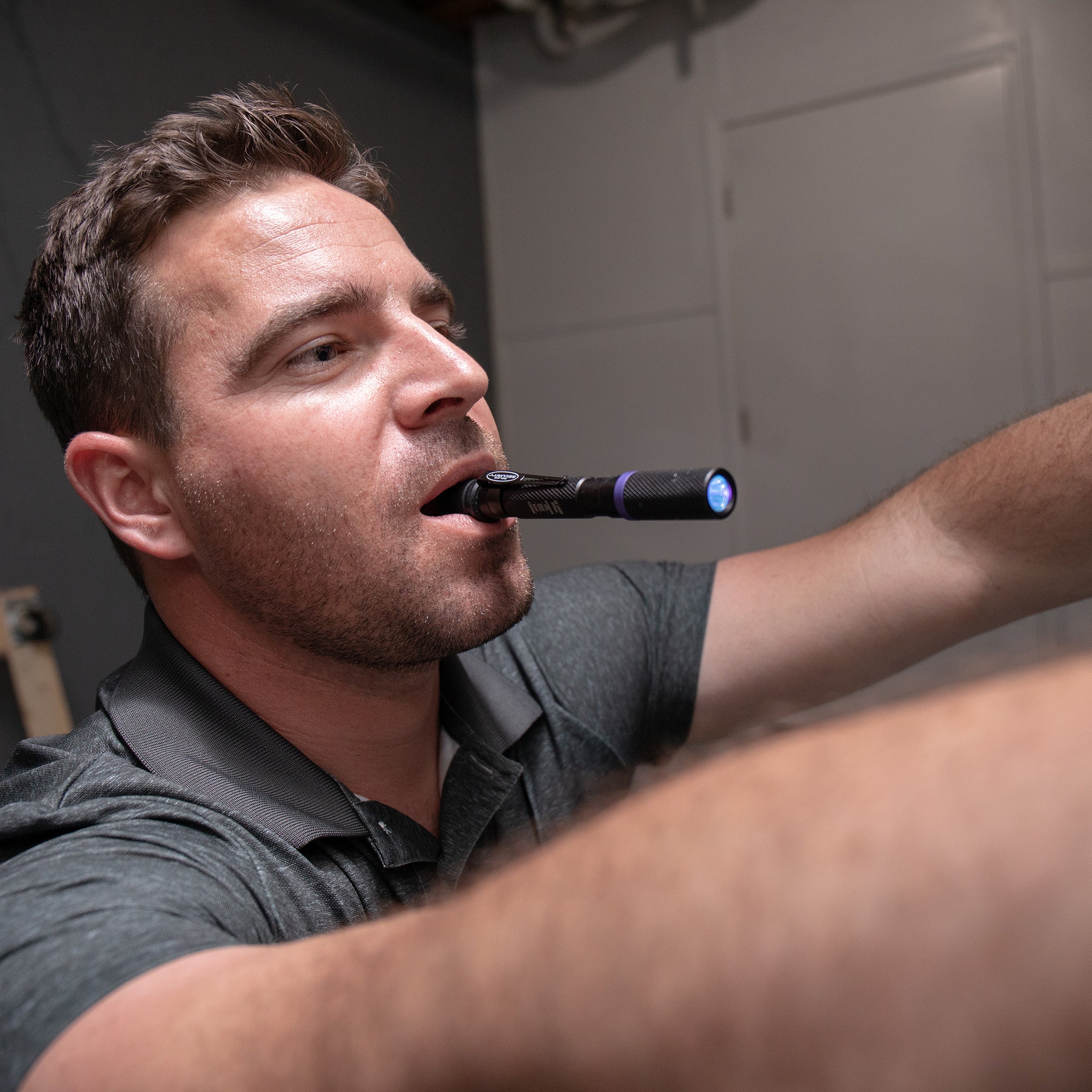 a man fixing something with the UV Inspection flashlight in his mouth pointing to where he's fixing