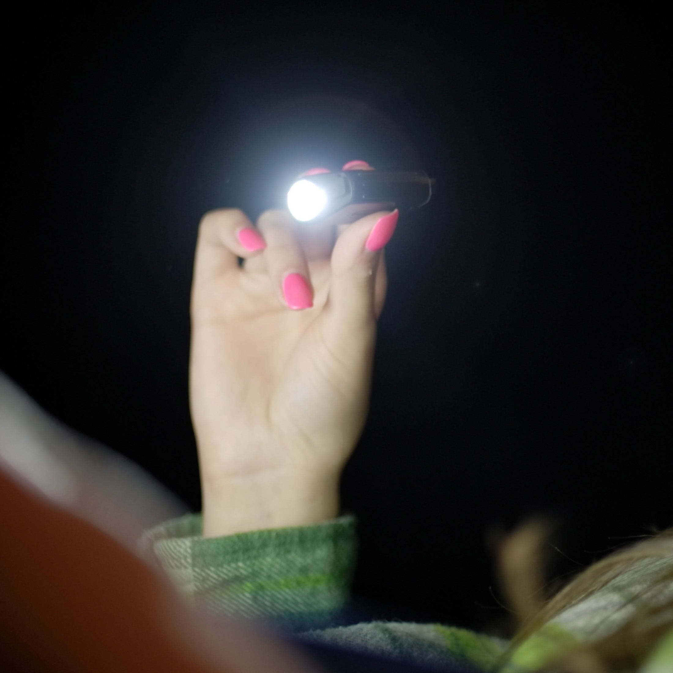 A female hand with pink nails holding a turned-on SEEKER-R Rechargeable Keychain Light