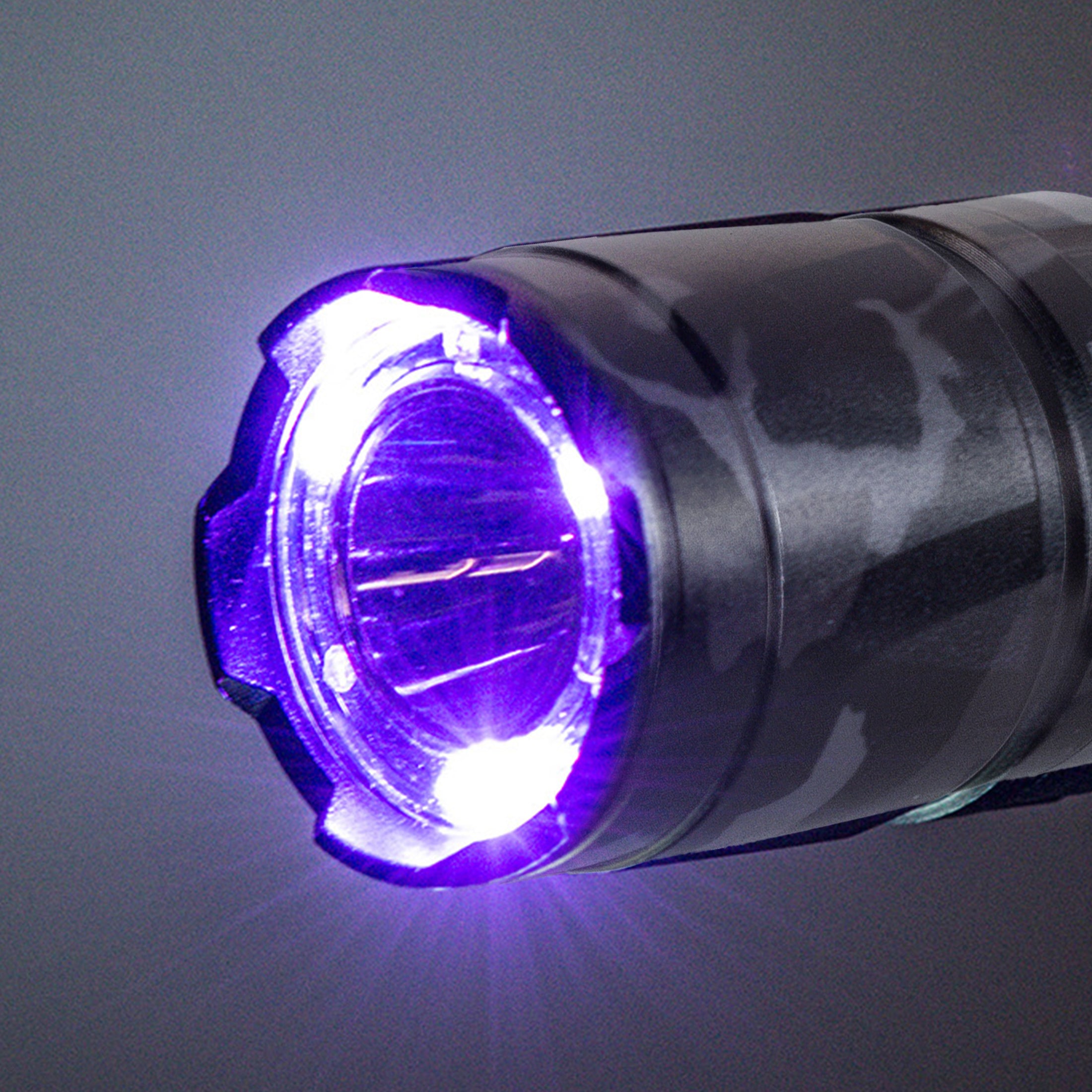 A close up shot of the lens of a tactical flashlight with the UV LEDs activated