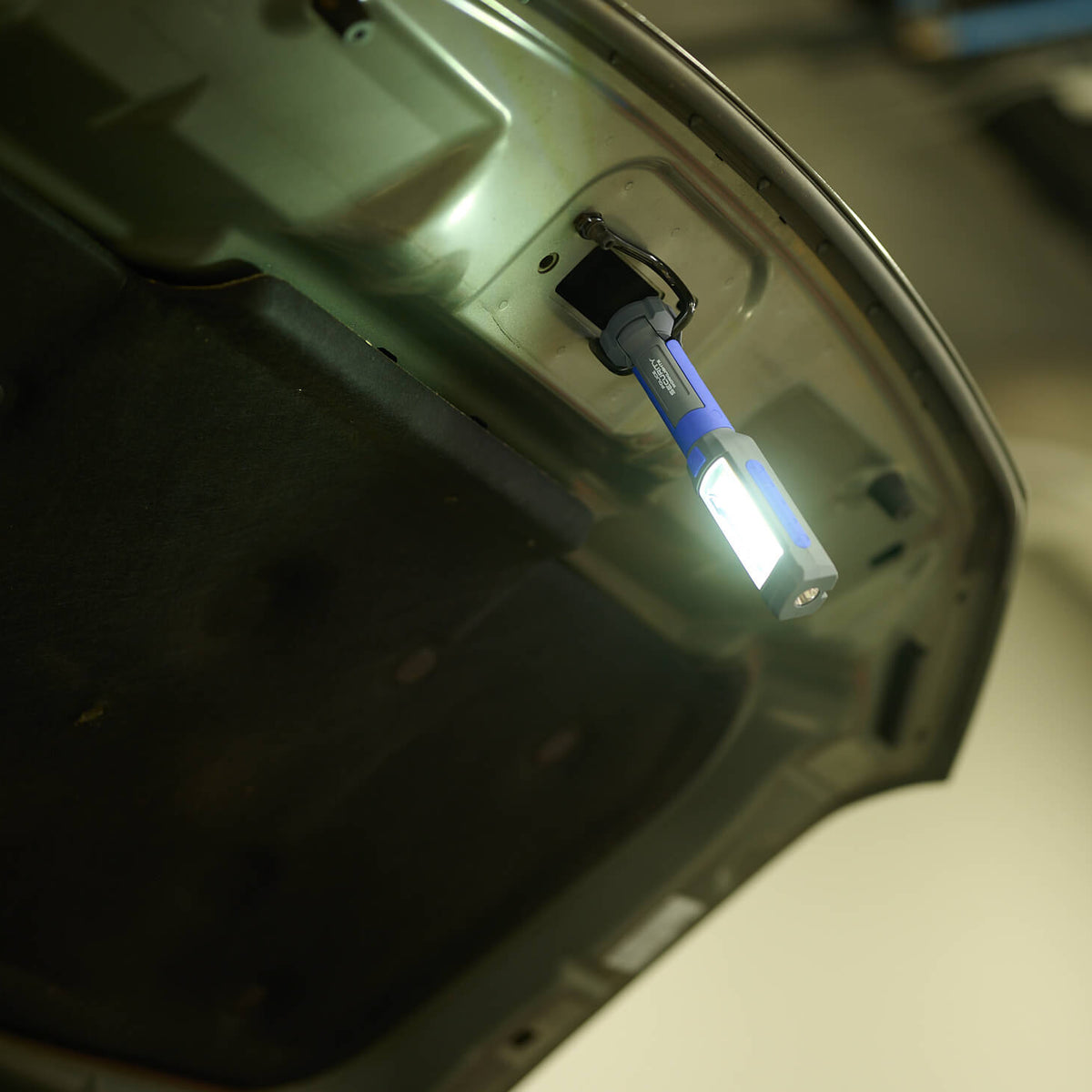 The Clamp Pro work light attached to the hook of a car hood to illuminate the engine bay.
