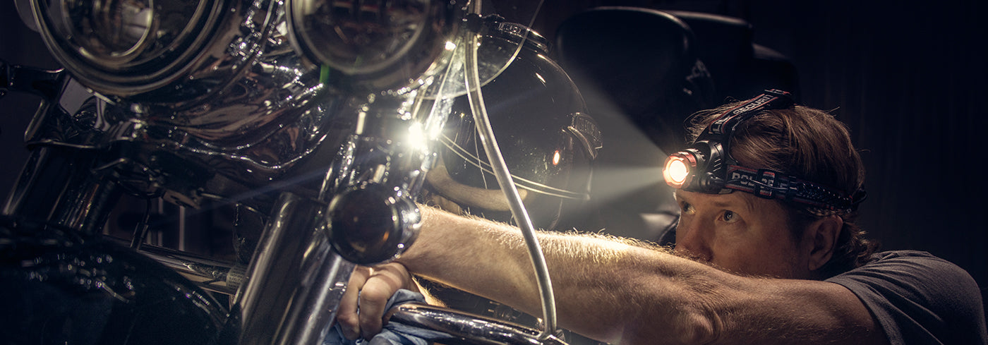 a large image of a man fixing his motorcycle while wearing a headlamp