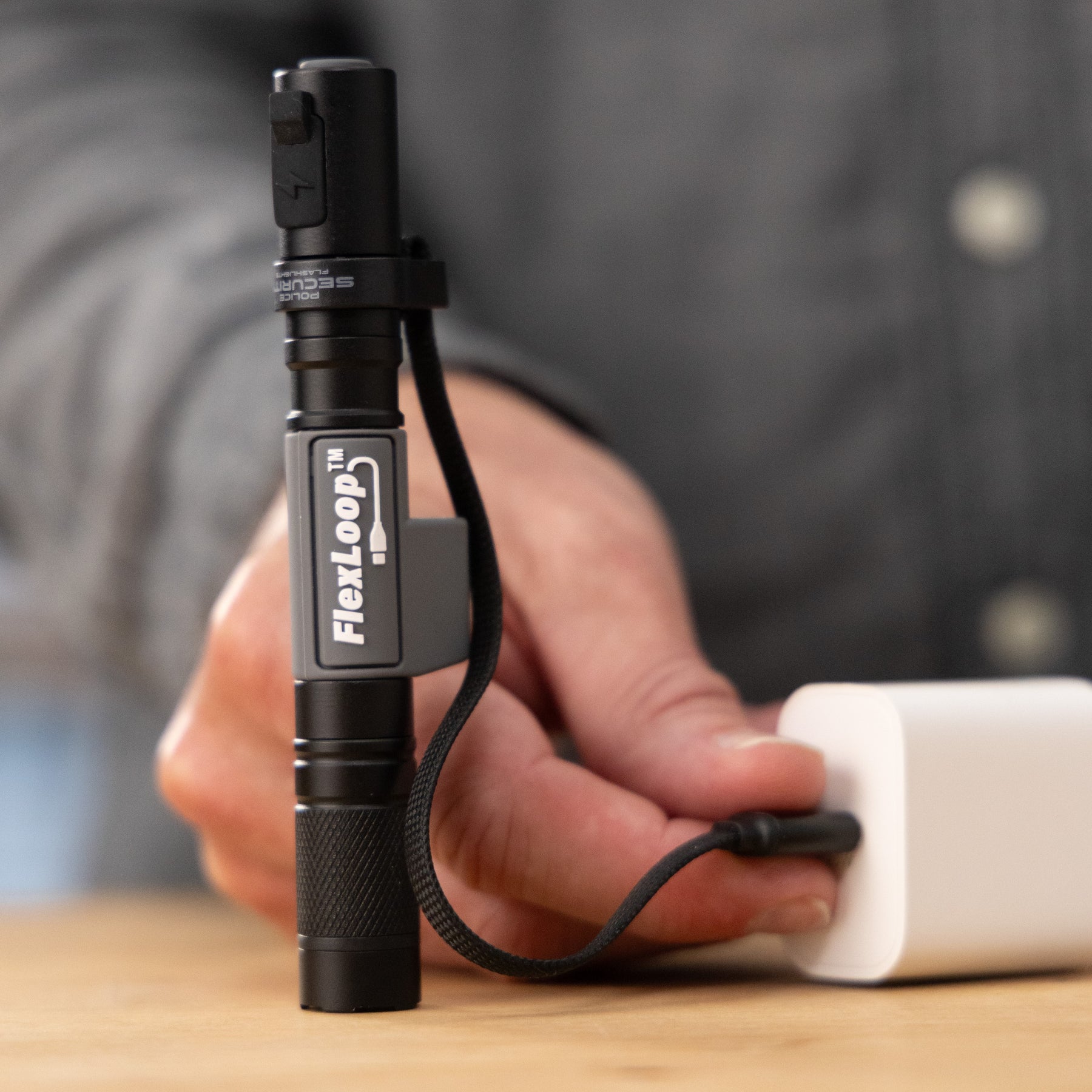 Person plugging in a black FlexLoop flashlight on a wooden surface.