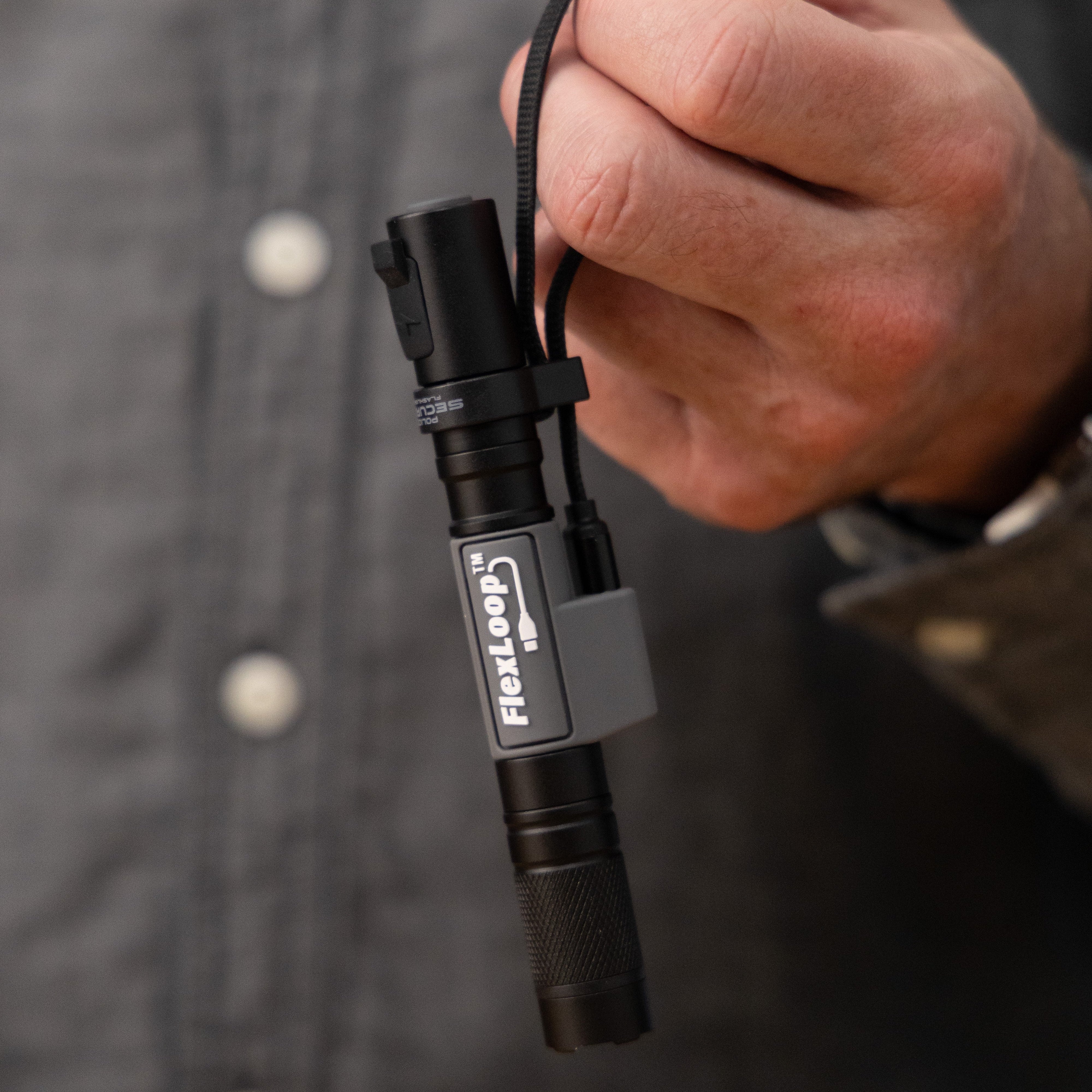 Hand holding a black flashlight with a visible brand logo against a dark background