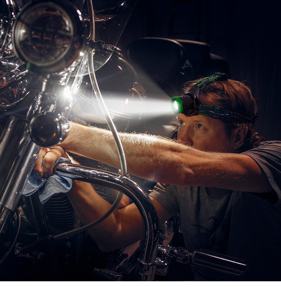 a man wearing a headlamp trying to fix his motorcycle