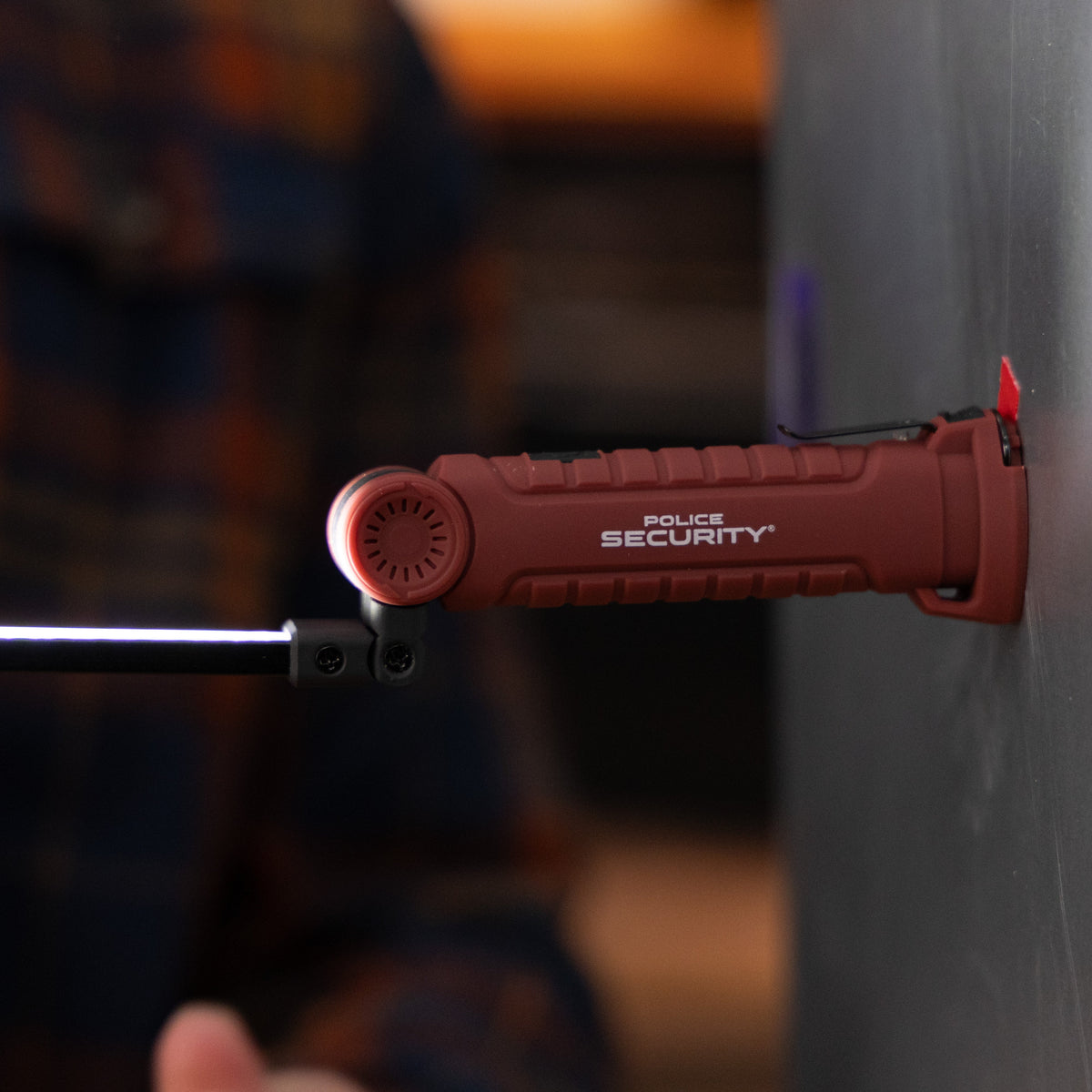 A Police Security ProFlex Mini worklight using its magnetic base to stick to a metal wall while the flexible COB arm shines upward