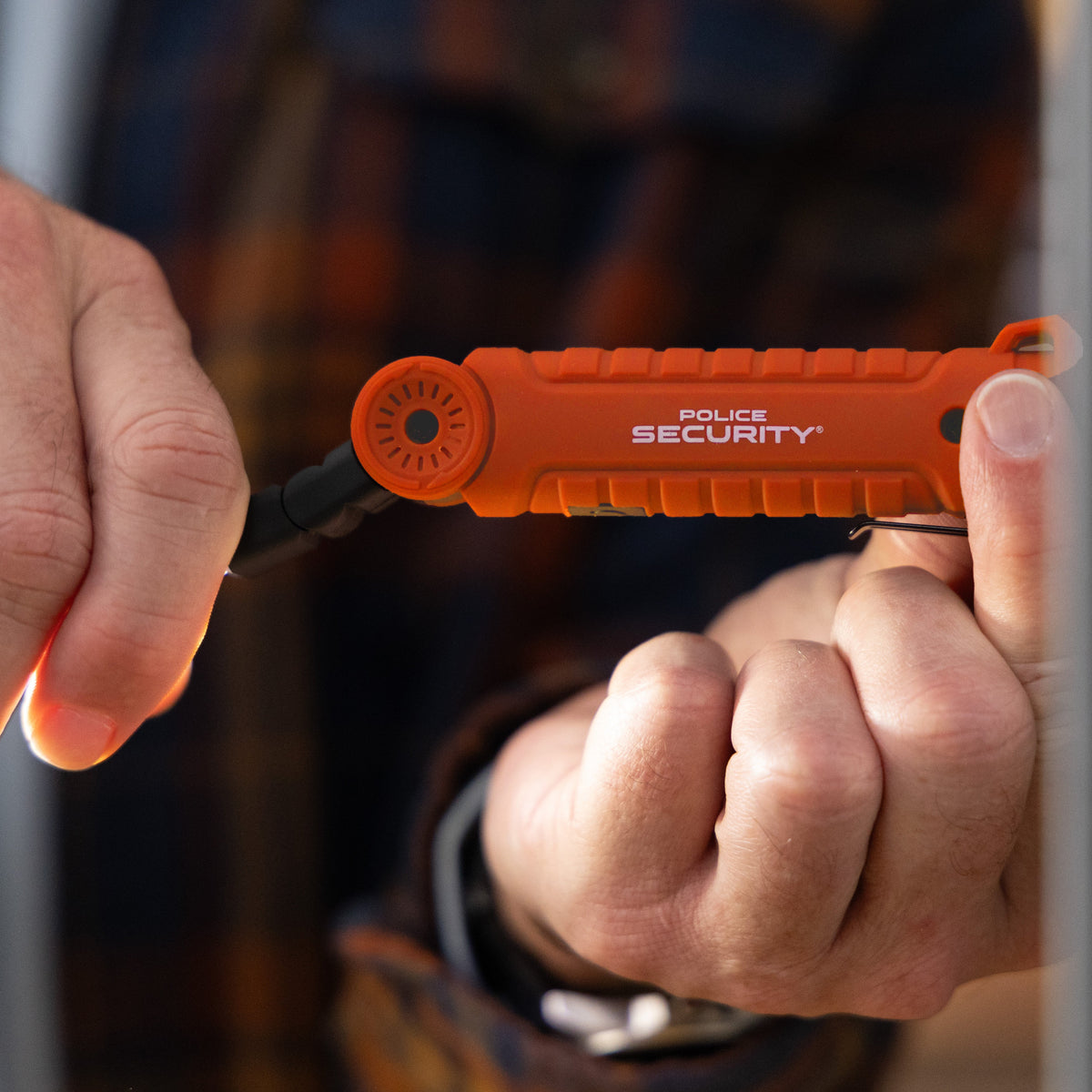 A close-up of a person's hands holding an orange Police Security worklight against a blurred background.