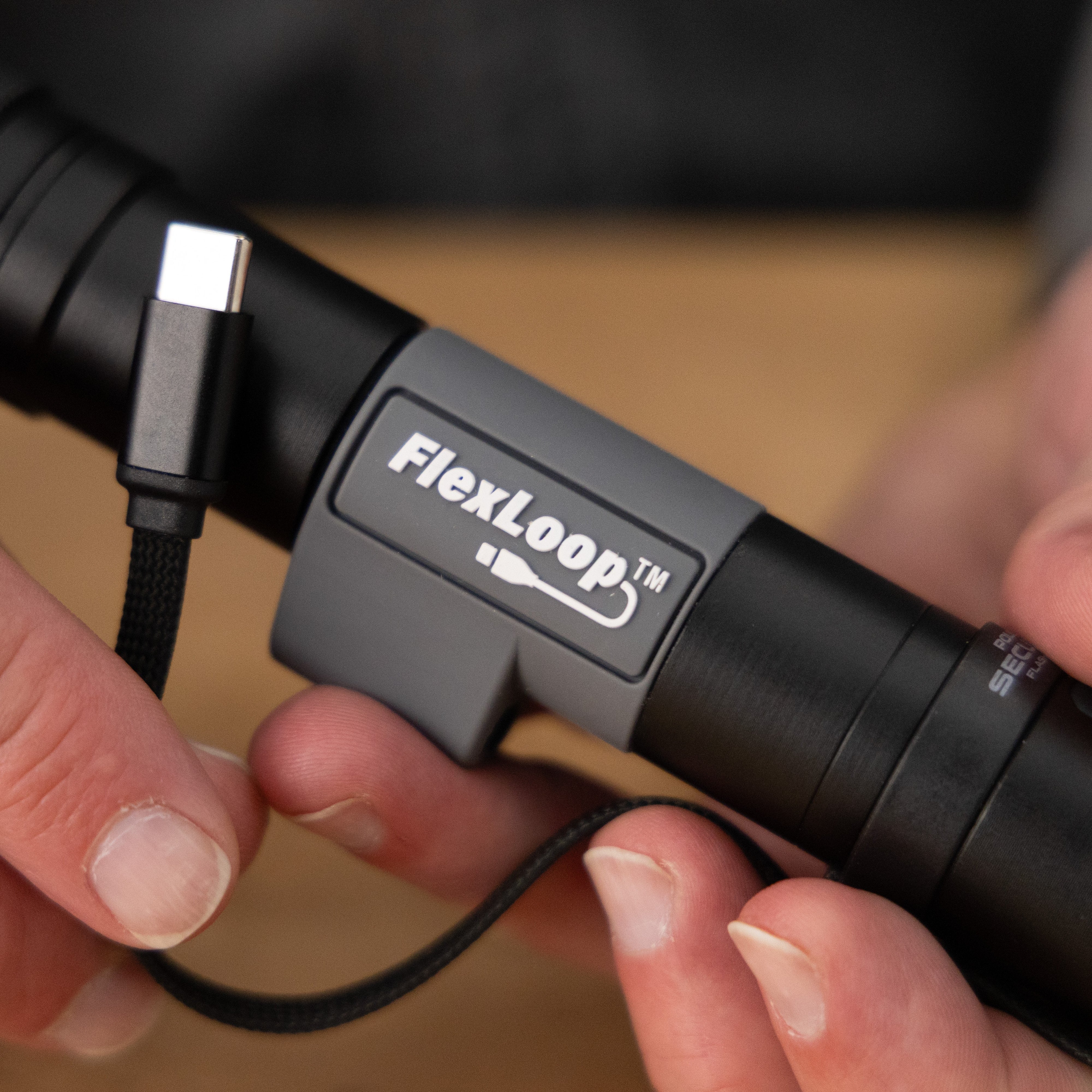 Person holding a FlexLoop Aura RX flashlight with a cable attached, on a blurred background