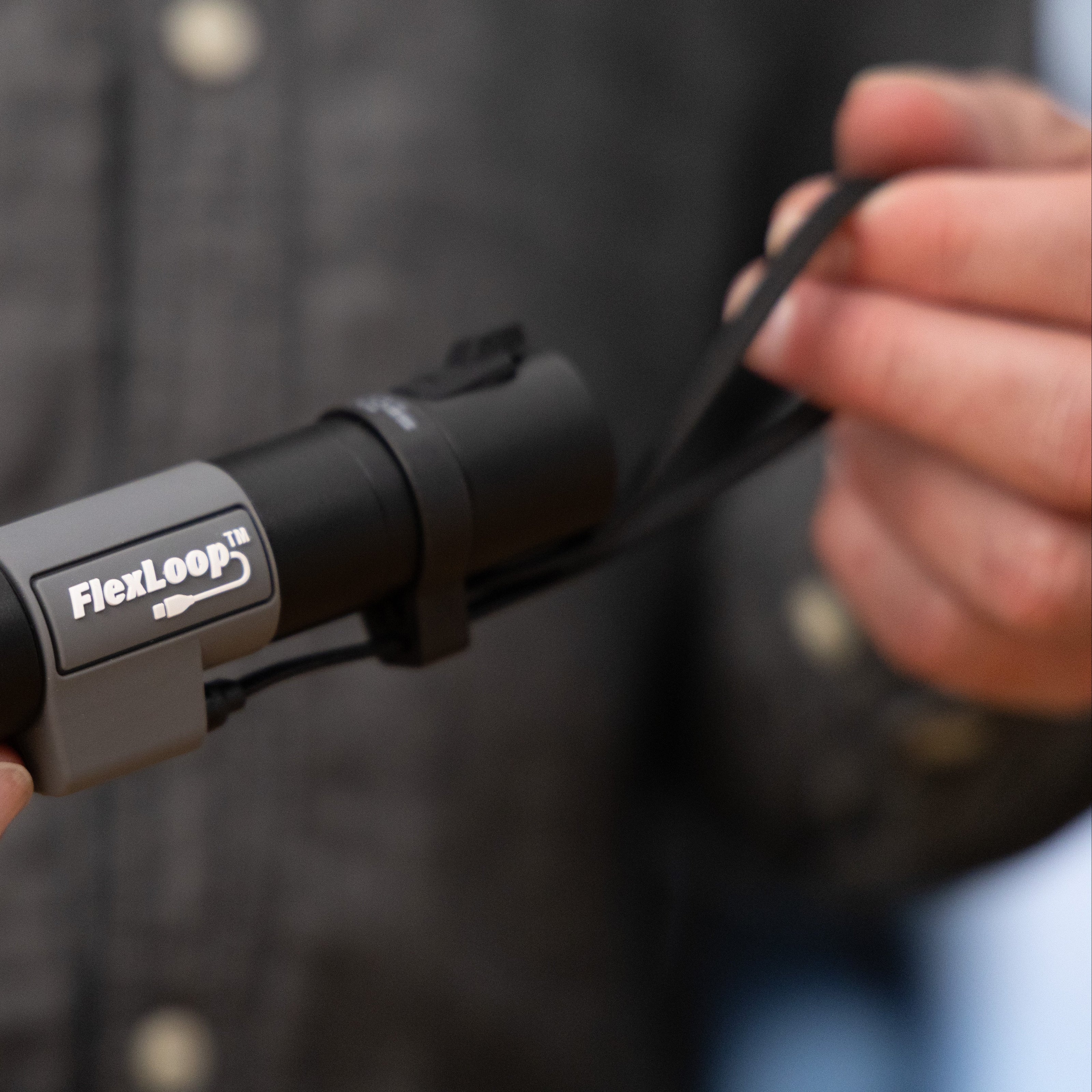 Person holding a black and gray FlexLoop Aura RX flashlight against a blurred background