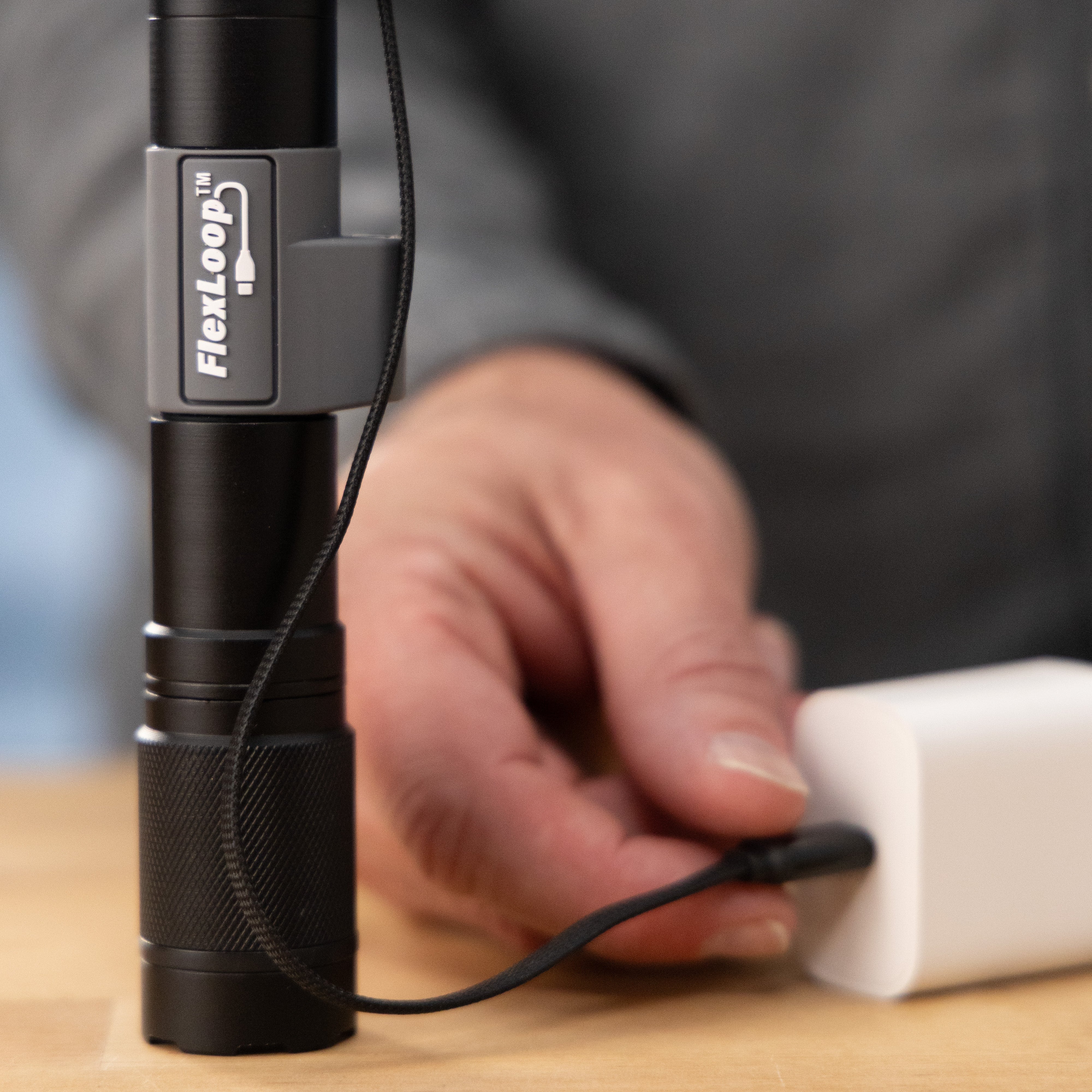 Black Aura RX flashlight with FlexLoop branding on a wooden surface, held by a hand.